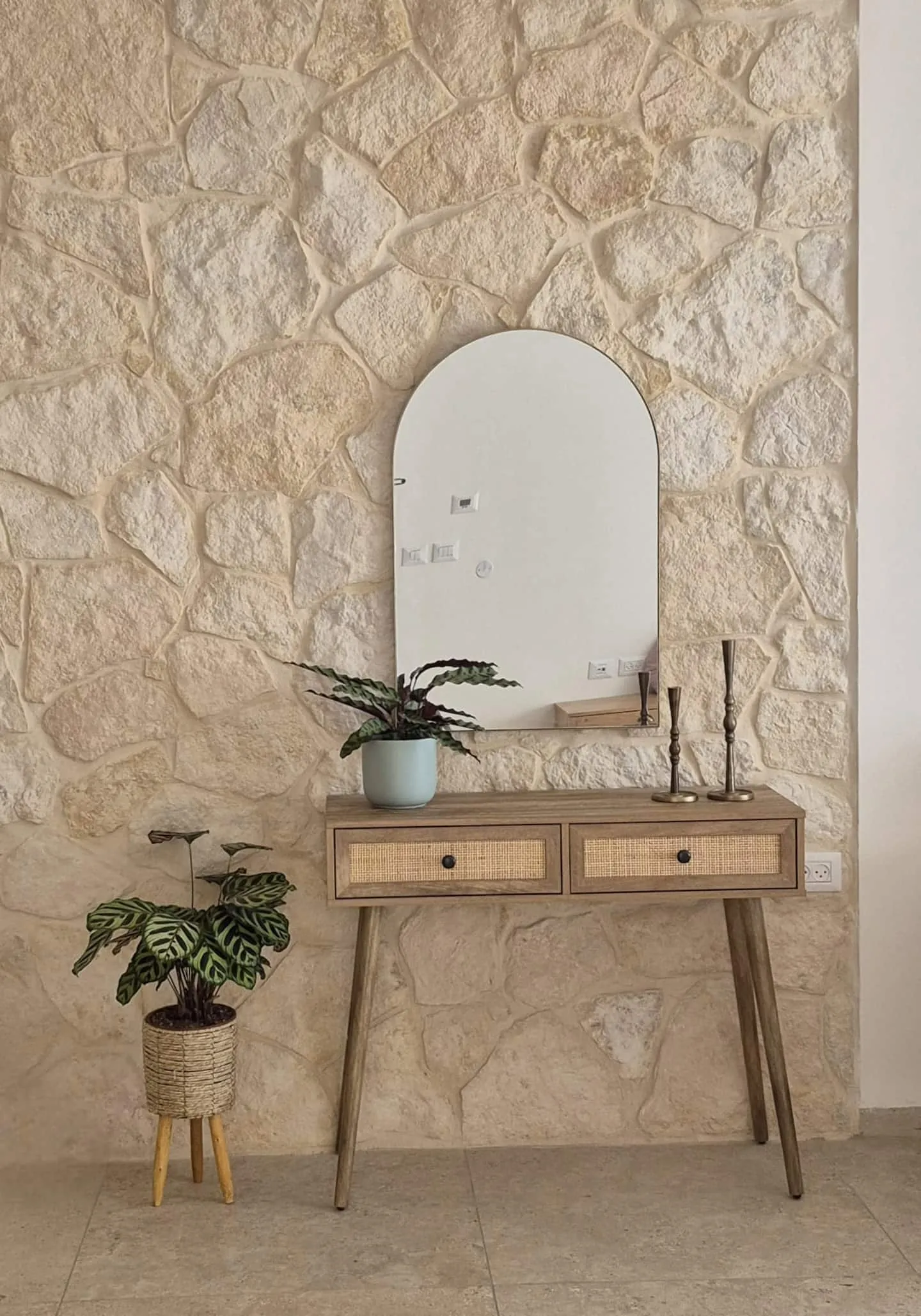 Entry console and an arched mirror against a stone wall.