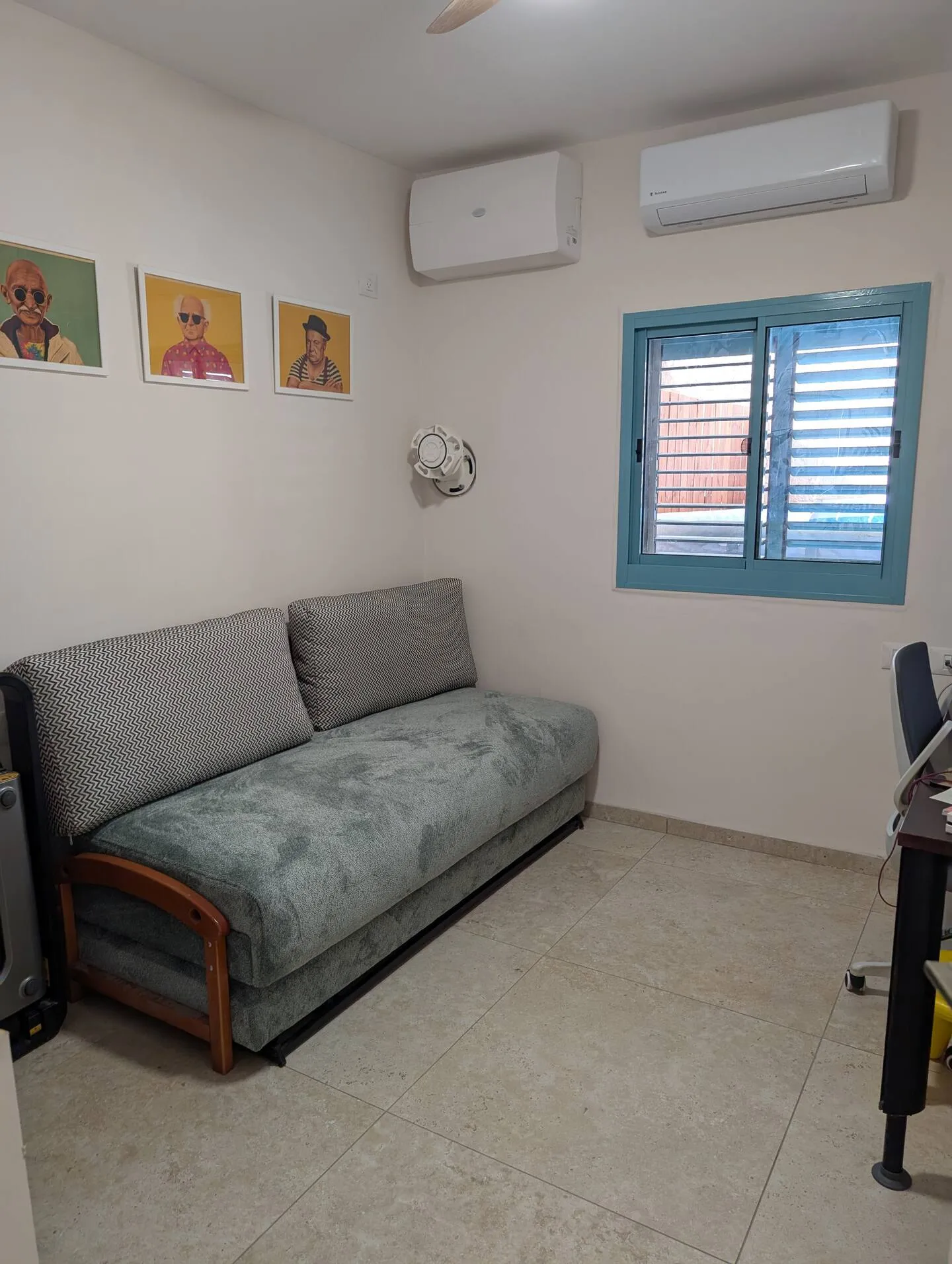 Room with a grey sofa bed, wall art, and a split air conditioner.