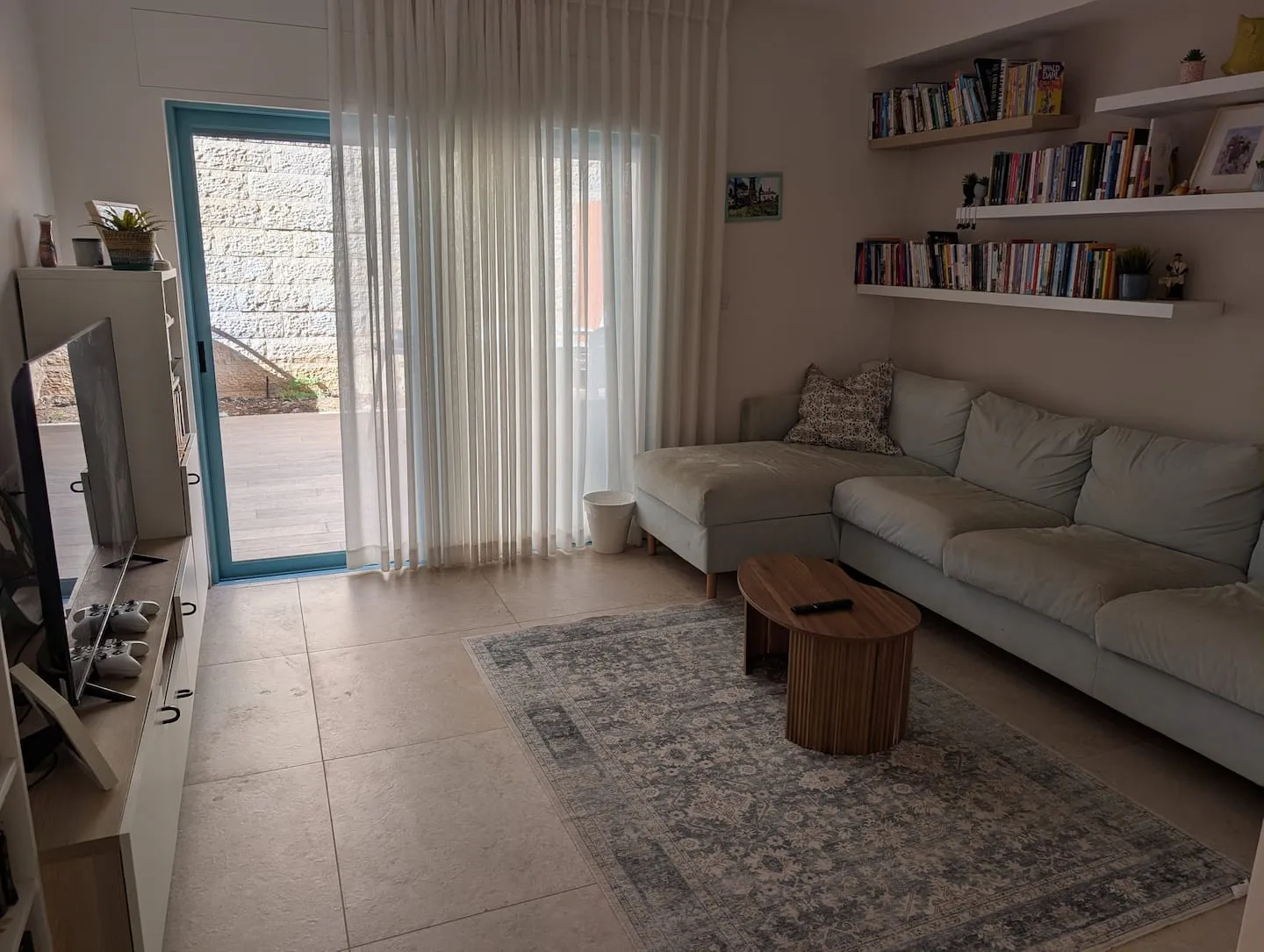 Living room with an L-shaped sofa, bookshelves, and a door toward the balcony.
